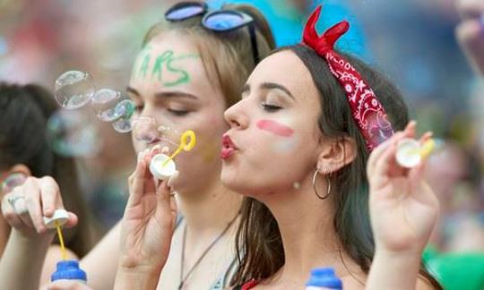 Two women with face paint blow bubbles with a bubble wand