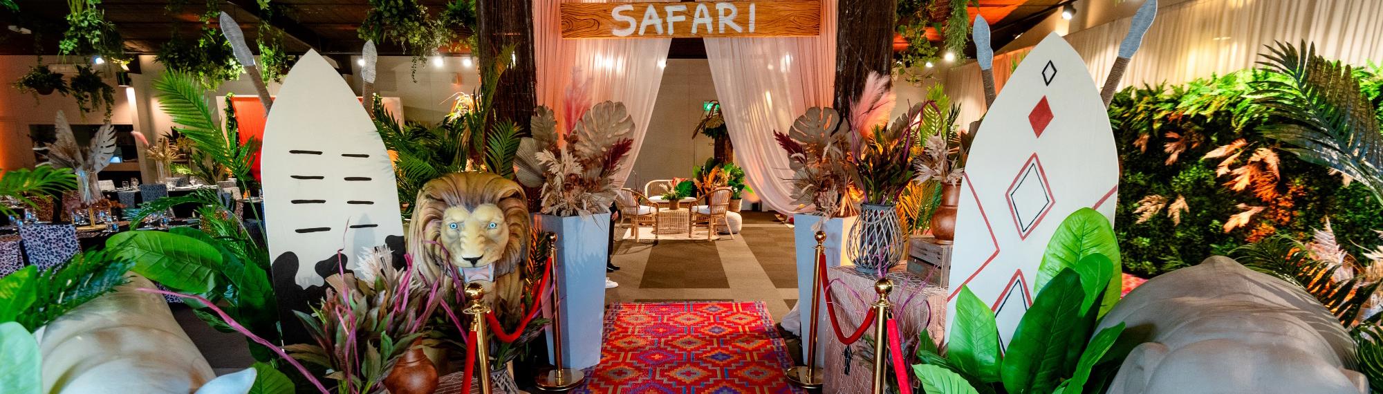 Inside the Leopard Lodge with a menagerie of tribal African and animal props in the foreground, a red carpet and white curtain with a "Safari" sign in the mid-ground, a furniture arrangement and guests in the background.