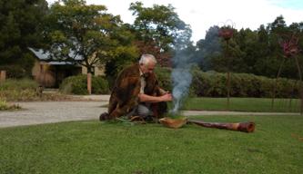 Elder Murrindindi taking part in a Cleansing Ceremony, with a burning grass pile and a didgeridoo.