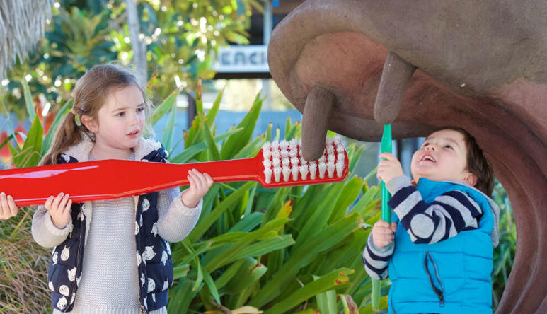 Three children brushing fake Hippo's tooth with a giant red toothbrush.