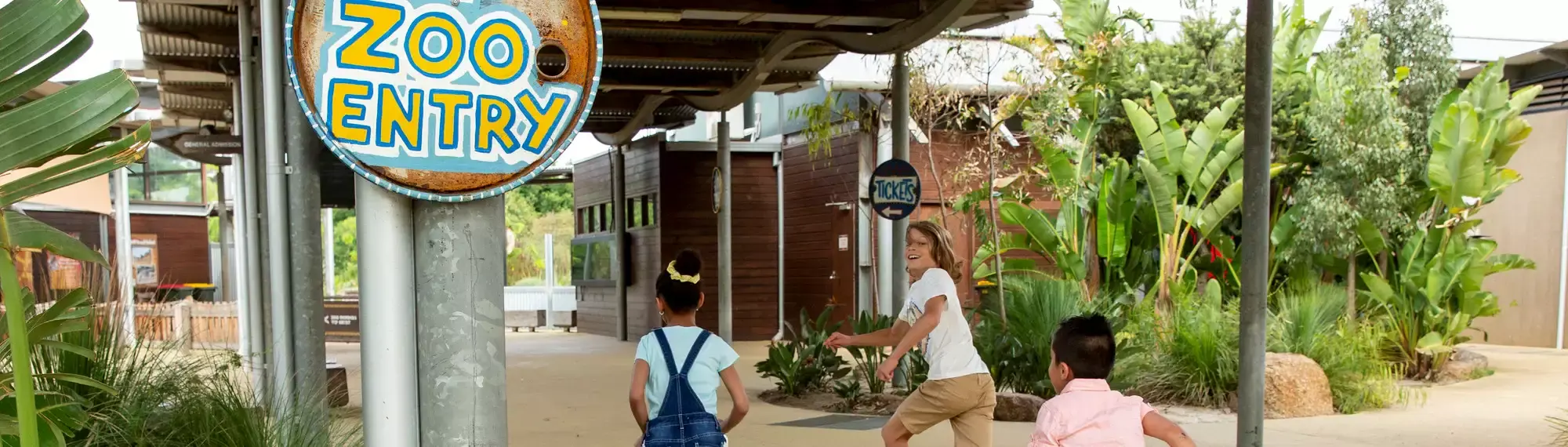 Three kids running past a sign that says "Zoo Entry."