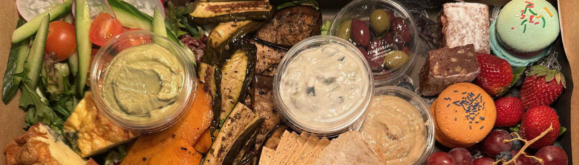 Hamper of assorted foods, including pumpkin, cheese, zucchini, cucumber, tomato, olives, bread, cherries, strawberries, cookies and macarons.