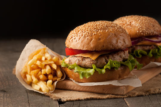 Two burgers and a bag of chips resting on a wooden chopping board