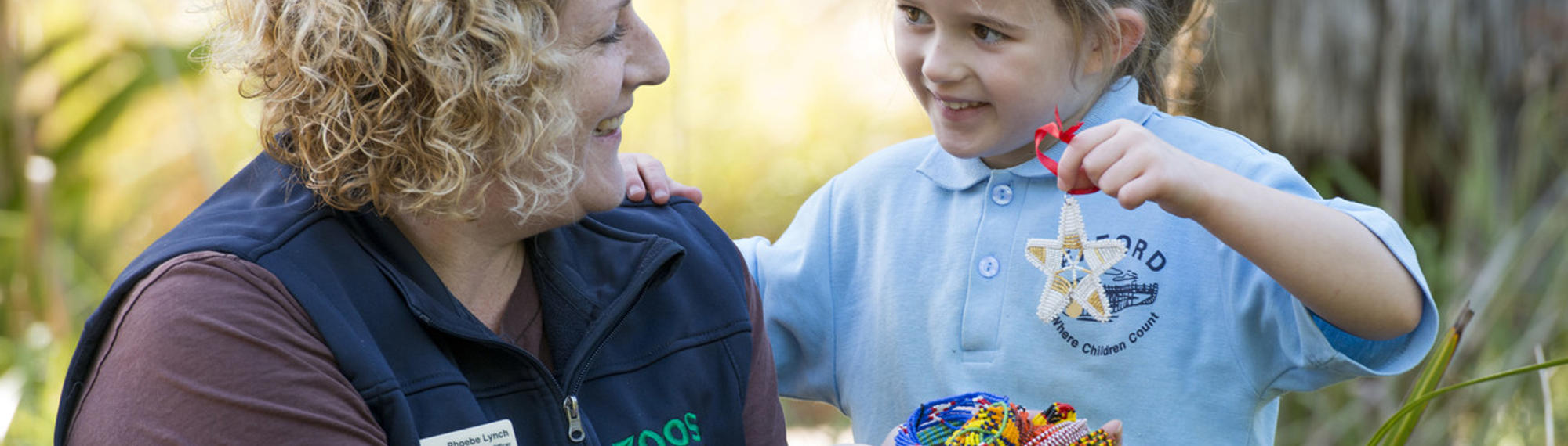 A Student with a ZV Educator, holding up her Beads for Wildlife craft creation.