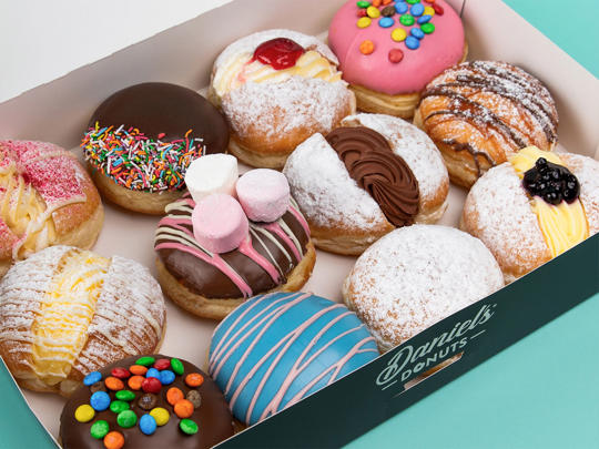 Twelve assorted donuts in a white and teal "Daniel's Donuts" box.
