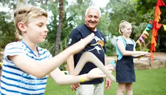 Two guests handling boomerangs, while an Elder looks on.