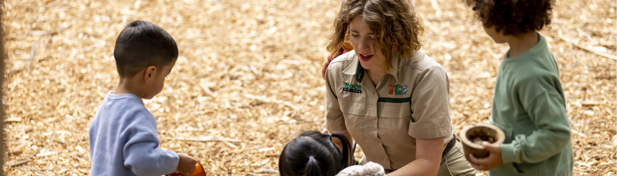 A Keeper interacts with four young guests in the bark-laden Adventure playground.
