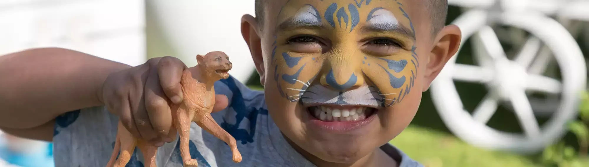 A young guest with tiger face-paint grins to the camera, while holding a lioness toy in his right hand.