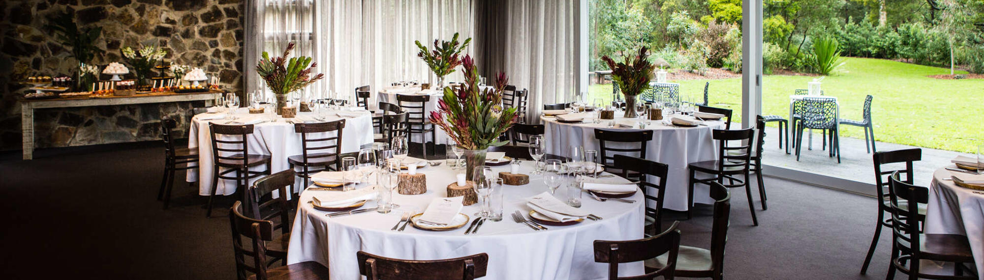 The Brogla room, set up with five dining tables, eight chairs per tables, a long table with snacks and flowers on it and two outdoor tables with four chairs each.