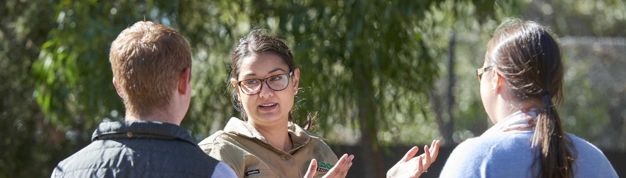 A Zoo keeper stands in front of two high school students in conversation.