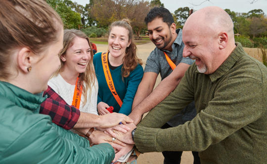 Five people are standing in a circle with their hands in the centre on top of each other.