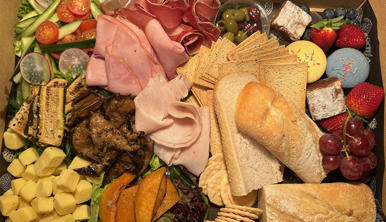 Hamper of assorted foods, including ham, turkey, cheese, zucchini, pastrami, tomato, olives, bread, cherries, strawberries, cookies and macarons.