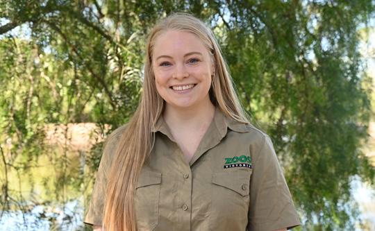 A Kyabram Fauna Park employee in uniform smiles, standing in front of the wetlands.