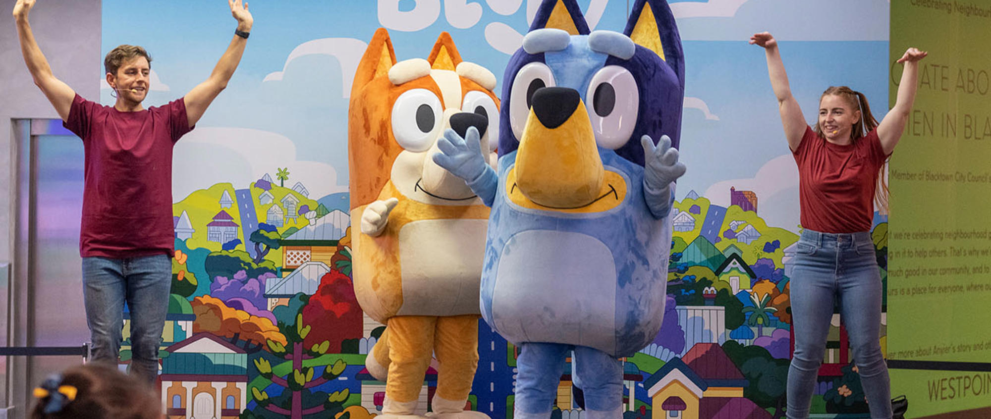 Bluey and Bingo mascots on stage with two performers standing with their arms up