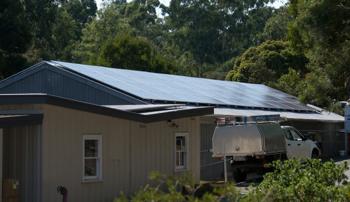 A ute parked next to a building with solar panels covering it's roof with trees behind the building