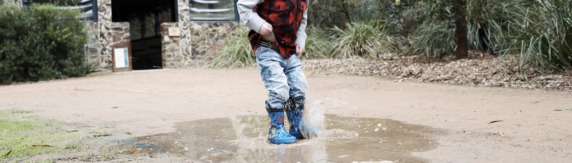A boy wearing blue gumboots lands in a puddle on the Sanctuary's path.