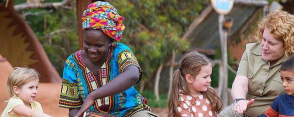 Three young guests sit with two women, one of whom is dressed in traditional colourful clothing and another in a Zoos Victoria uniform.