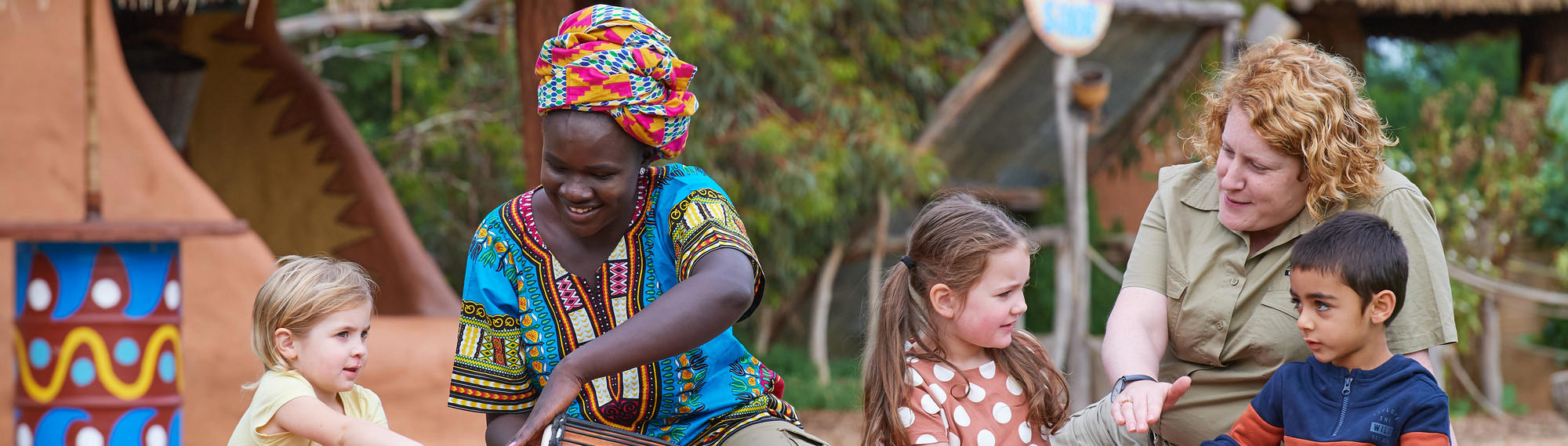 Three young guests sit with two women, one of whom is dressed in traditional colourful clothing and another in a Zoos Victoria uniform.