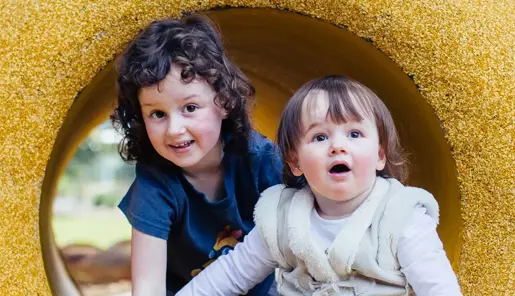 Two children crawling in a yellow tunnel, looking toward the camera.