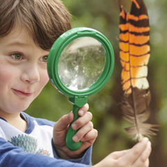 Kinder Keeper Kid examines a brown-and-orange feather with a green magnifying glass.