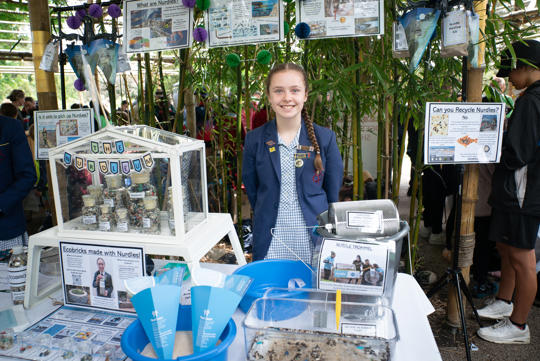 A school student stands smiling behind her craft showcase.