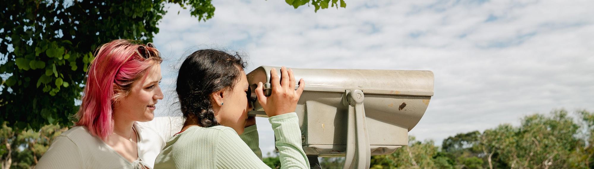 Side view of two guests as they look to the right through lookout binoculars.