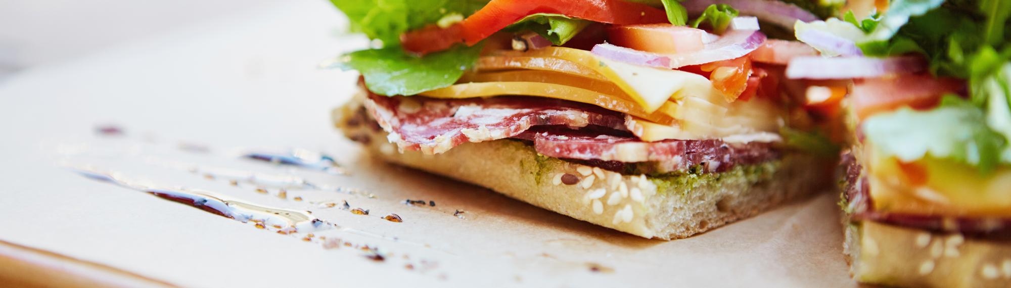 Close-up of a sandwich made of salami, cheese, tomato, red onion and lettuce, on wholegrain bread.
