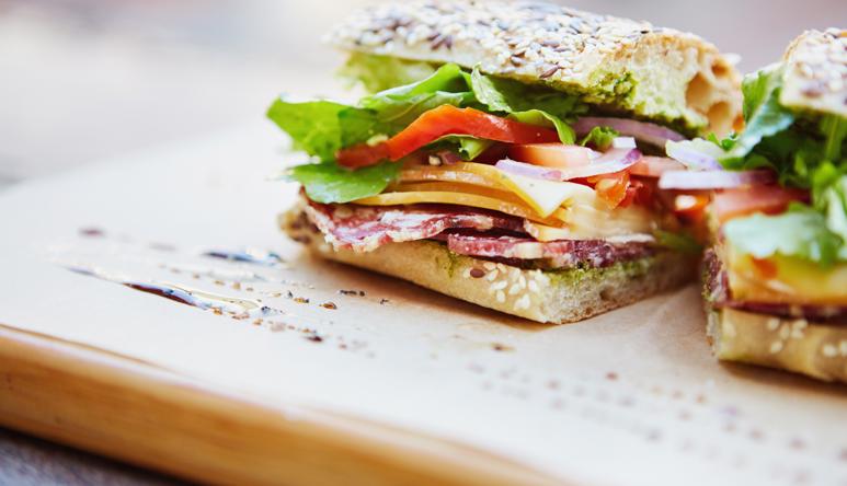 Close-up of a sandwich made of salami, cheese, tomato, red onion and lettuce, on wholegrain bread.