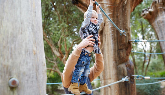 A young guest joyfully grabbing onto a thick, blue rope, while his parent is behind him, holding him up.