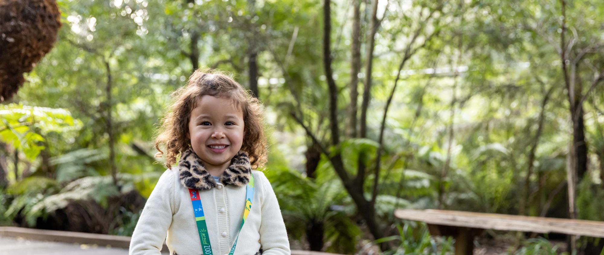 Young guest holding her Zoo Member lanyard, on the Koala Walk, smiling to the camera.