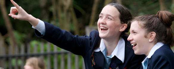 Two students smile as one points into the air.