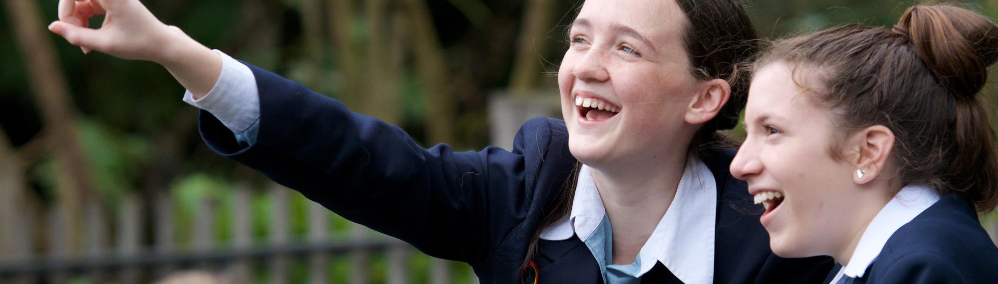 Two students smile as one points into the air.