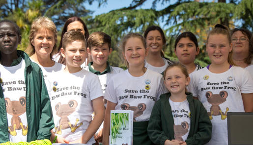 A group of 11 students and 3 Zoo staff, standing in a row, smiling and wearing shirts saying "Save the Baw Baw Frog."