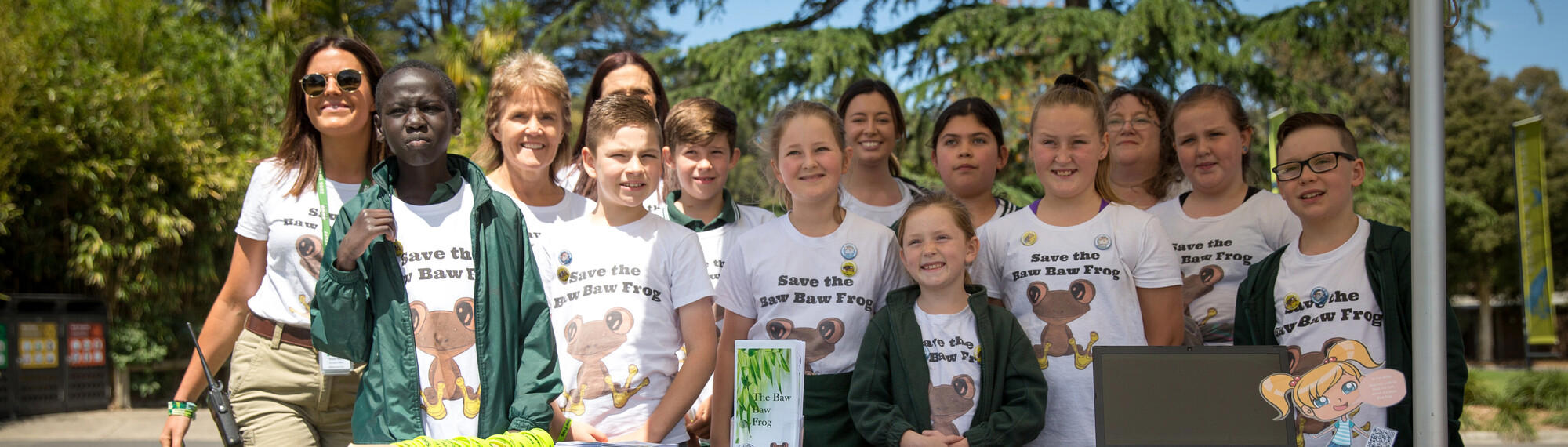 A group of 11 students and 3 Zoo staff, standing in a row, smiling and wearing shirts saying "Save the Baw Baw Frog."