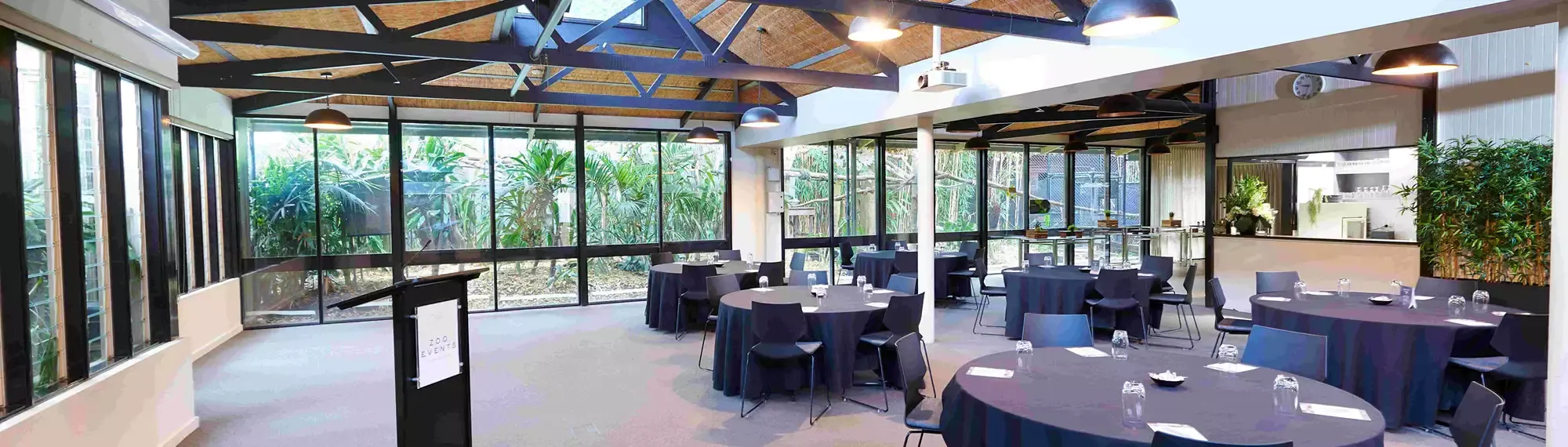 A wide-shot of the Bong Su Room, with the lectern and six tables with chairs surrounding them.