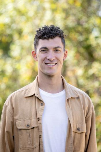 Portrait of Ryan McDonough, smiling to the camera in front of a leafy backdrop.