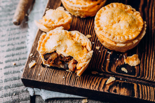 Some party pies resting on a wooden board. One has had a bite taken out of it.