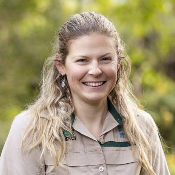 Keeper Jessica, smiling to the camera in front of a leafy backdrop.
