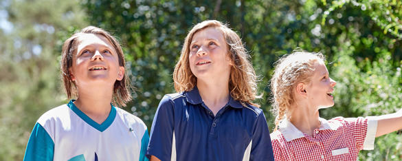 Three students smile as they walk through the bush on a sunny day.